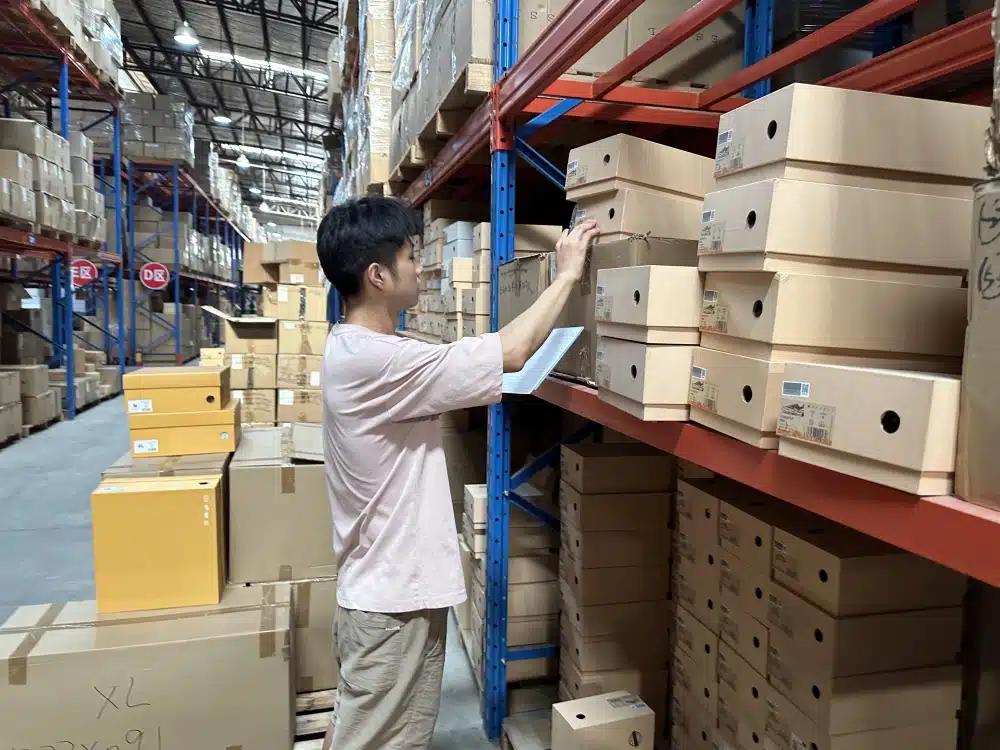 Warehouse worker checking shoebox inventory against a clipboard in a China 3PL warehouse