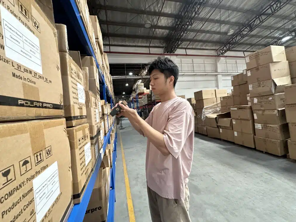 Worker inspecting a small packaged product beside labeled cartons in a China fulfillment warehouse