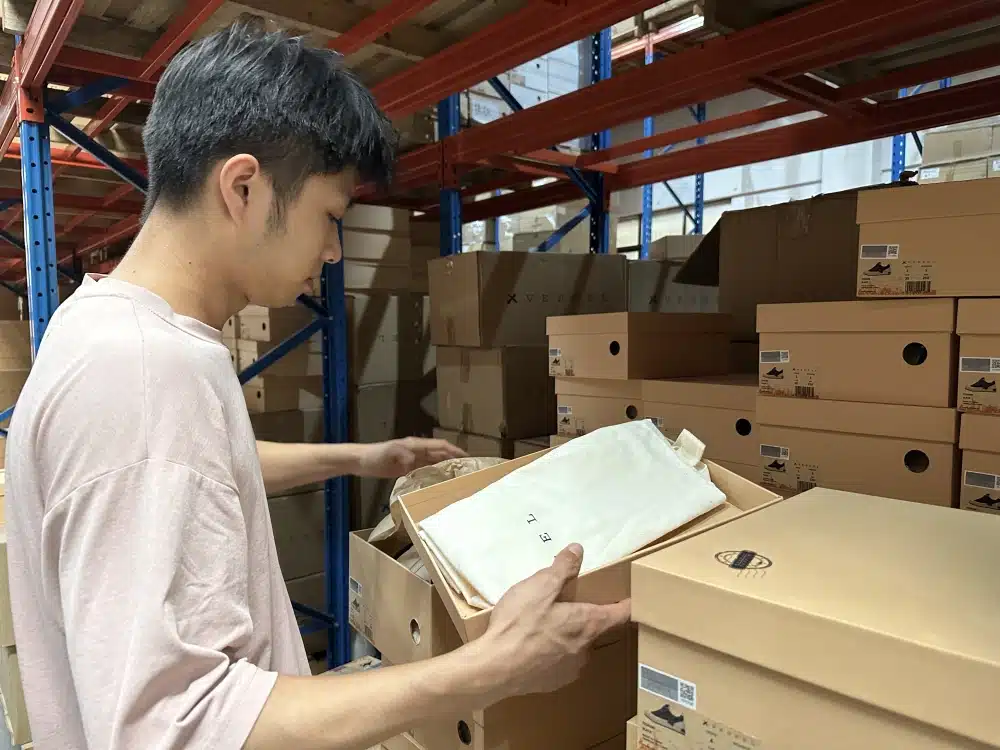 Warehouse employee checking labeled shoebox inventory against a clipboard in a China 3PL storage area