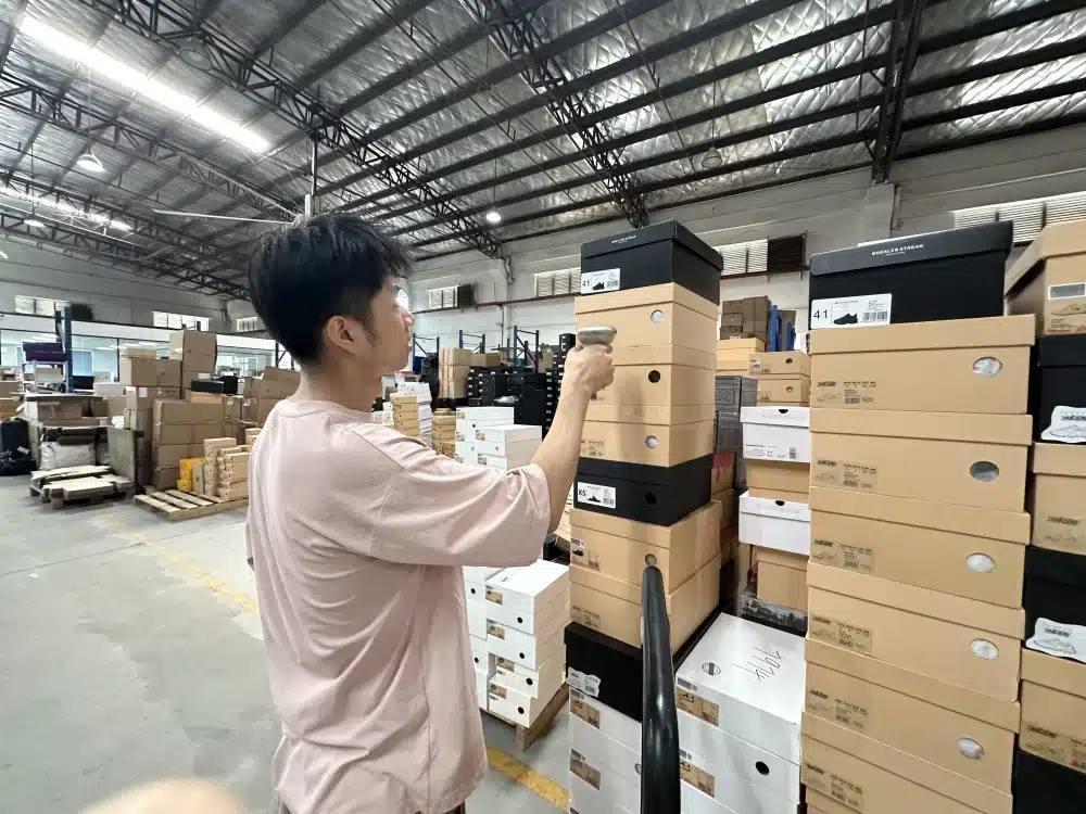Worker checking an open shoebox and fabric bag in a China fulfillment warehouse