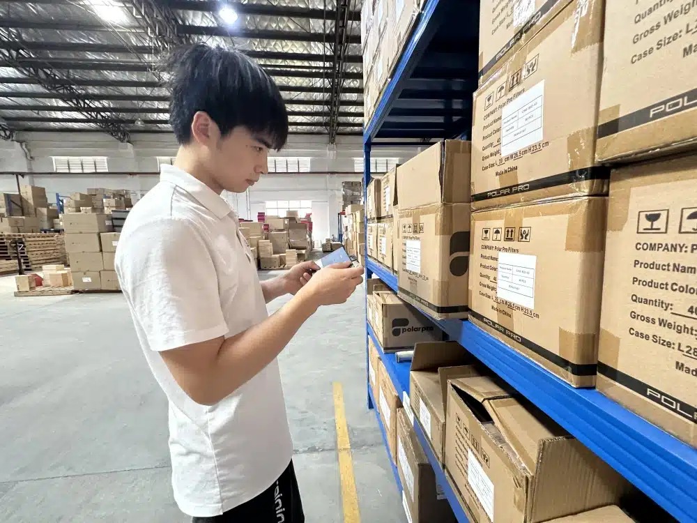 Warehouse worker examining a small boxed item beside labeled cartons as part of Q4 inventory verification