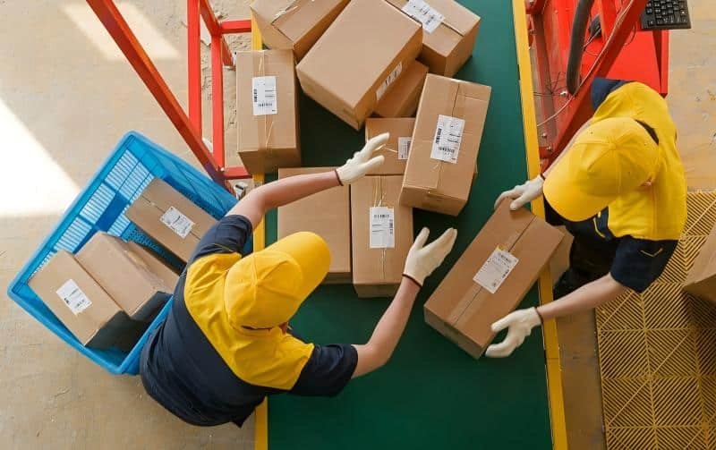 Warehouse workers sorting and labeling late pledge orders on a conveyor belt for separate fulfillment