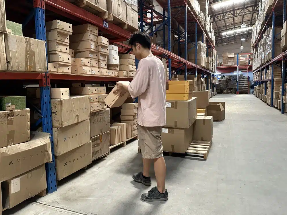 Warehouse worker handling a shoebox beside storage racks, illustrating labor behind ecommerce fulfillment costs