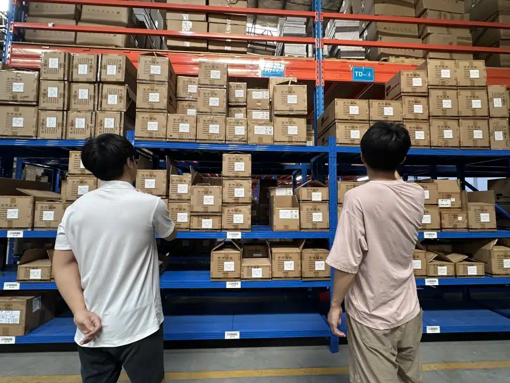 Two warehouse workers reviewing labeled inventory cartons on blue storage shelves in China