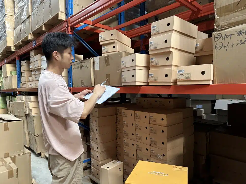 Warehouse worker recording stock counts on a clipboard beside labeled shoeboxes in a China 3PL facility