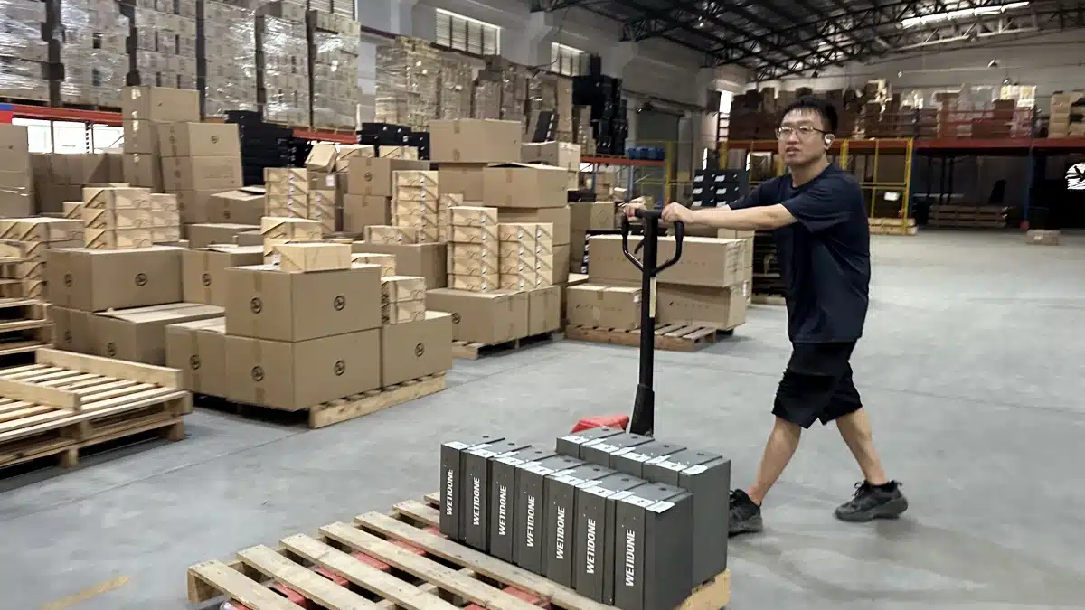 Warehouse worker moving palletized inventory with a pallet jack, illustrating inventory handling and operational costs included in fulfillment cost per order.