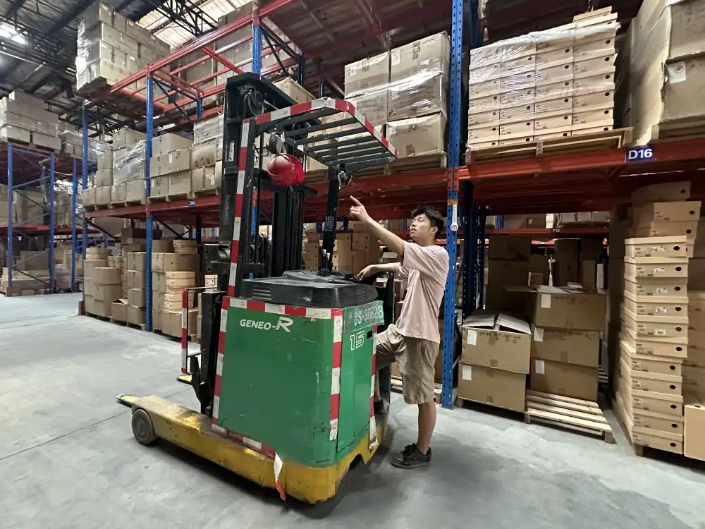 Warehouse worker operating a forklift to manage palletized inventory as part of total landed cost from China to USA