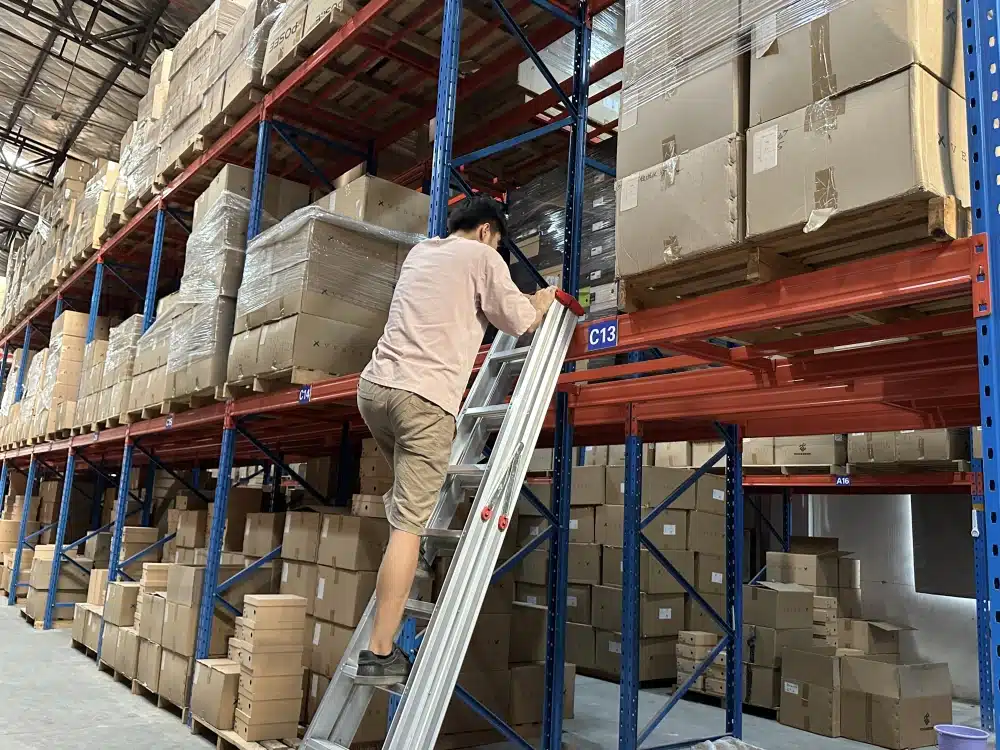 Warehouse worker climbing a ladder beside palletized cartons on tall storage racks in China