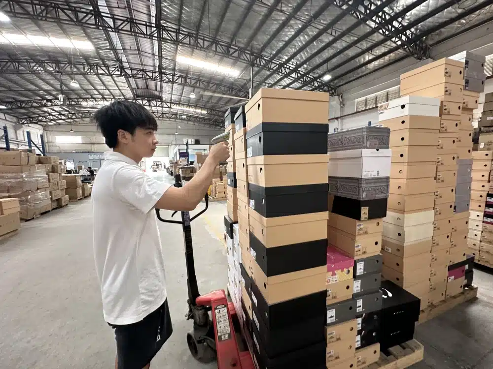 Warehouse employee scanning stacked shoebox barcodes to verify inventory for WooCommerce fulfillment