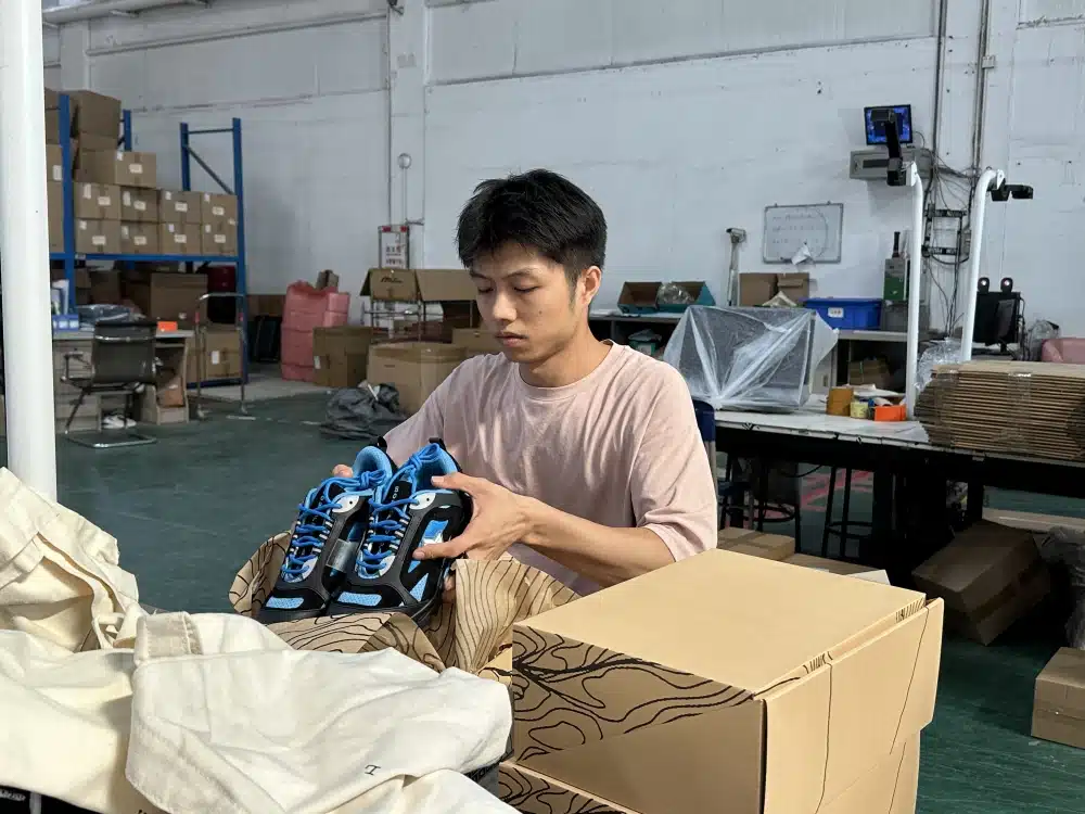 Warehouse worker checking a shoebox beside stacked inventory during WooCommerce order fulfillment preparation