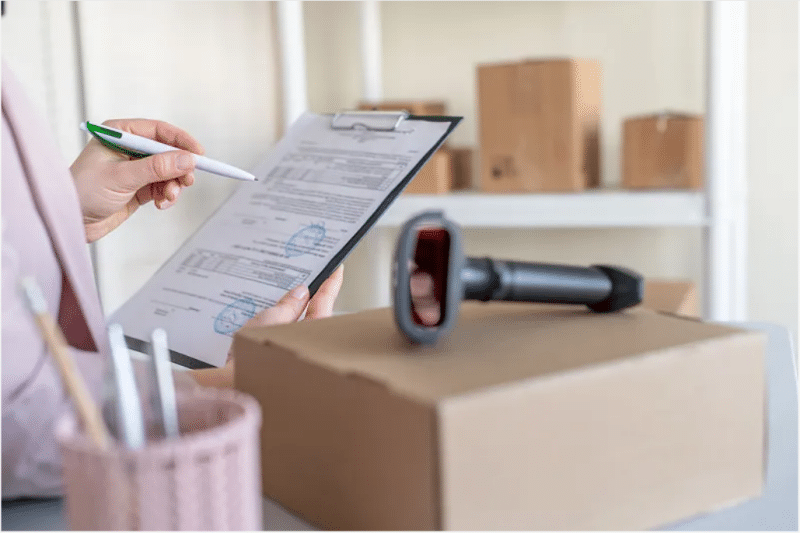 Business professional reviewing shipping invoices and cost sheets with a clipboard and scanner, analyzing peak season surcharges and budget variances.