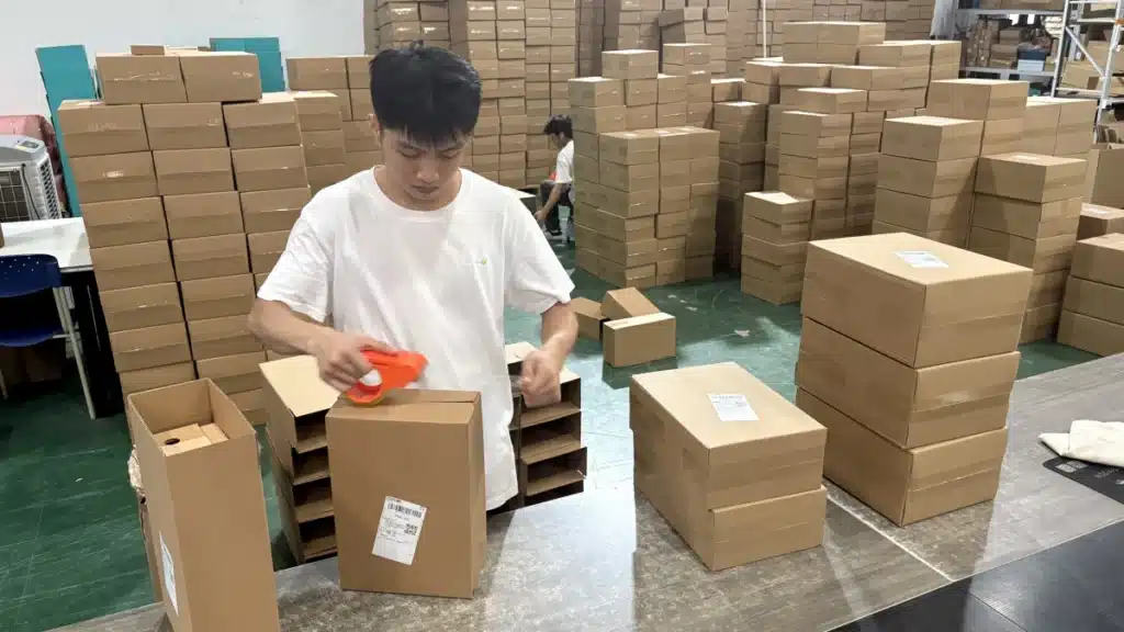 Fulfillment worker sealing an individual ecommerce parcel at a packing station, illustrating direct-to-consumer fulfillment and small-order pick and pack operations.