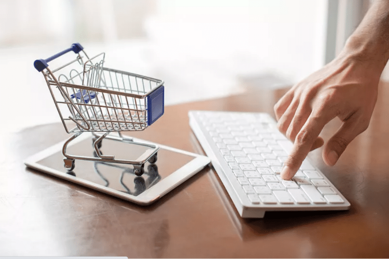 Hand typing on keyboard next to tablet displaying miniature shopping cart, illustrating e-commerce order processing and centralized inventory control for multi-channel sales.