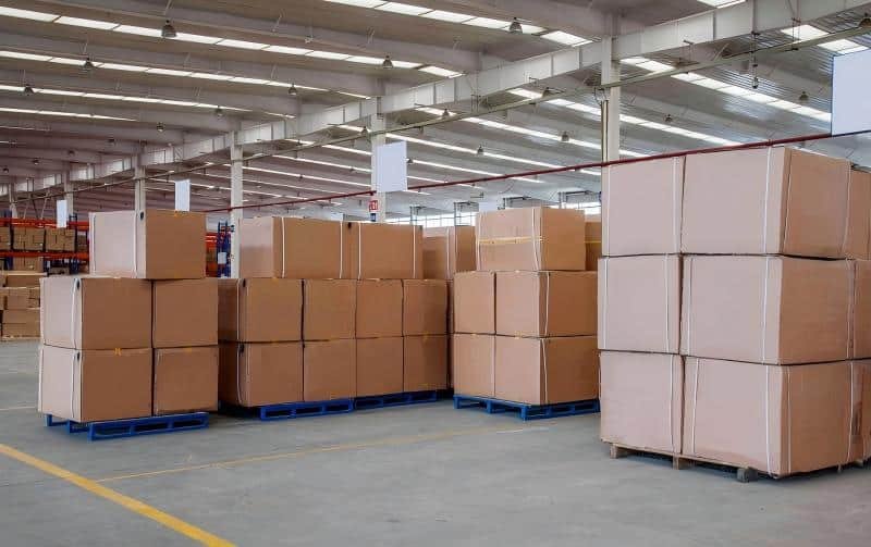 Stacks of cardboard boxes on blue pallets inside a large fulfillment center warehouse, illustrating inventory storage costs.