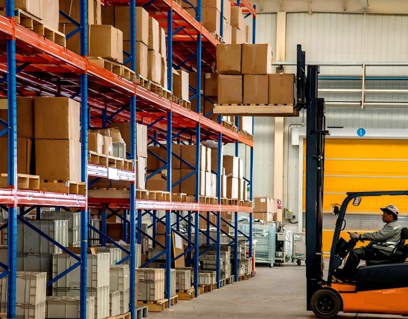 Warehouse worker operating a forklift to move pallets onto high racks, illustrating the labor and equipment costs behind fulfillment services.
