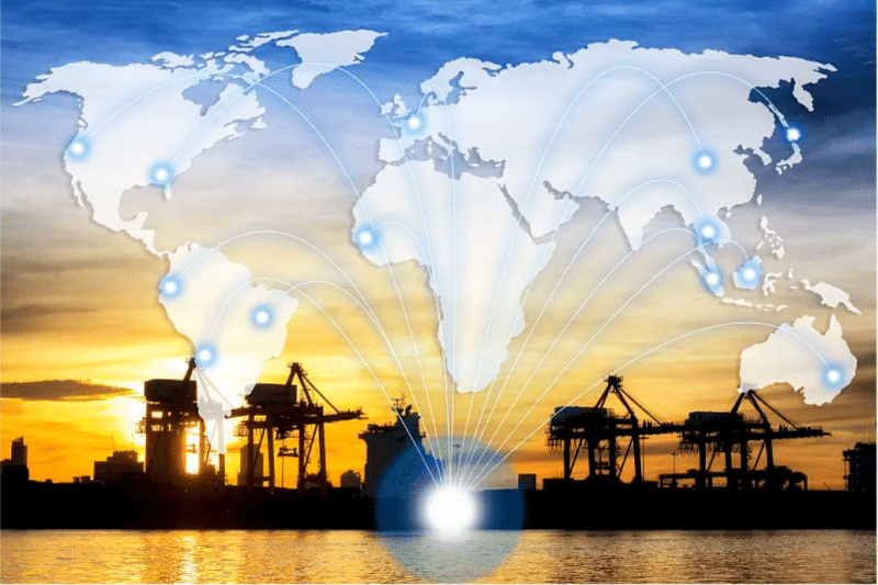 Silhouette of a container port at sunset with a glowing world map overlay showing global shipping routes, representing international logistics infrastructure for omnichannel retail fulfillment.