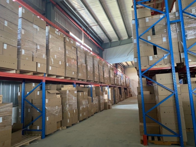 Aisle in a large fulfillment warehouse filled with stacked cardboard boxes on industrial shelving, representing slow-moving inventory that may incur long-term storage charges.