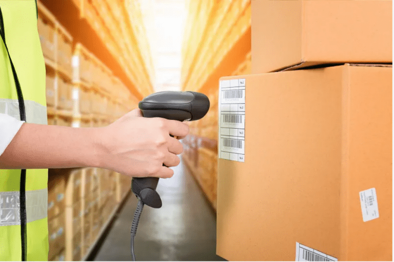 Warehouse worker in a safety vest scanning a barcode on a package in a busy distribution center during the holiday rush.
