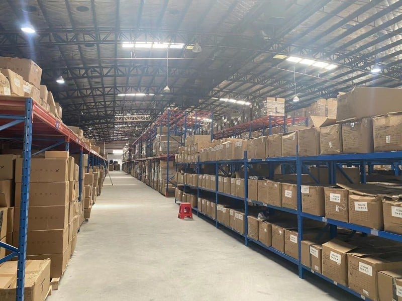 Long aisle in a fulfillment warehouse filled with labeled cardboard boxes on industrial shelving, representing staged components ready for custom subscription box assembly based on customer preferences or seasonal themes.