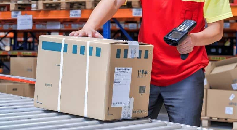 Close-up of a warehouse worker scanning a barcode on a shipping box, highlighting the pick and pack fees associated with fulfillment.