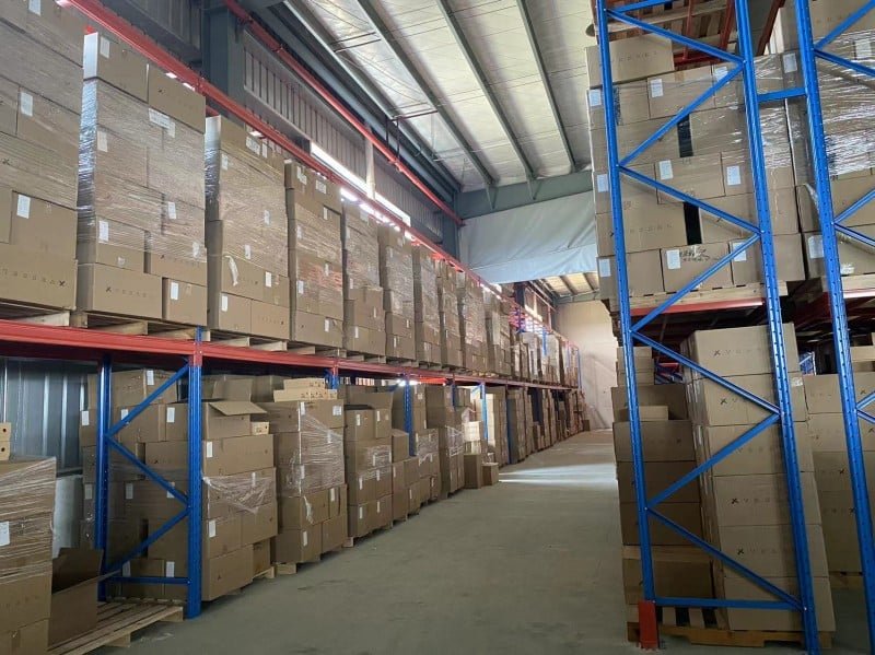 Aisle view of a fulfillment center with towering blue-and-red pallet racks fully loaded with shrink-wrapped cartons, representing pre-staged inventory ready for rapid dispatch during high-volume flash sale events.