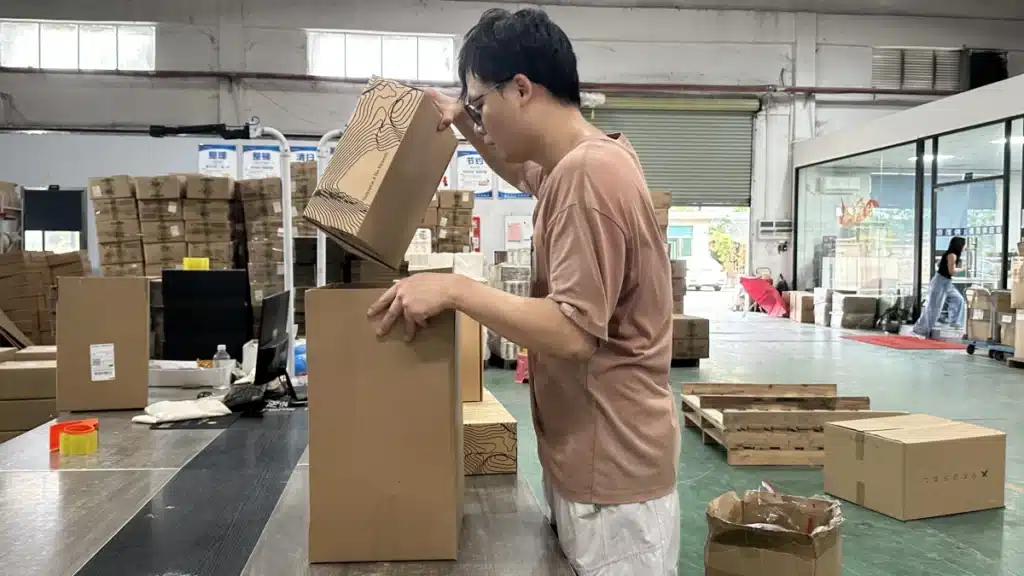 Warehouse worker packing multiple product boxes into a larger shipping carton, demonstrating wholesale fulfillment and bulk order processing for retailers and distributors.