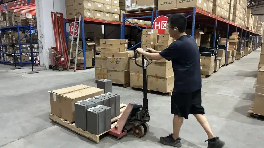 Warehouse worker moving palletized inventory with a pallet jack as part of professional warehousing company operations and inventory handling.