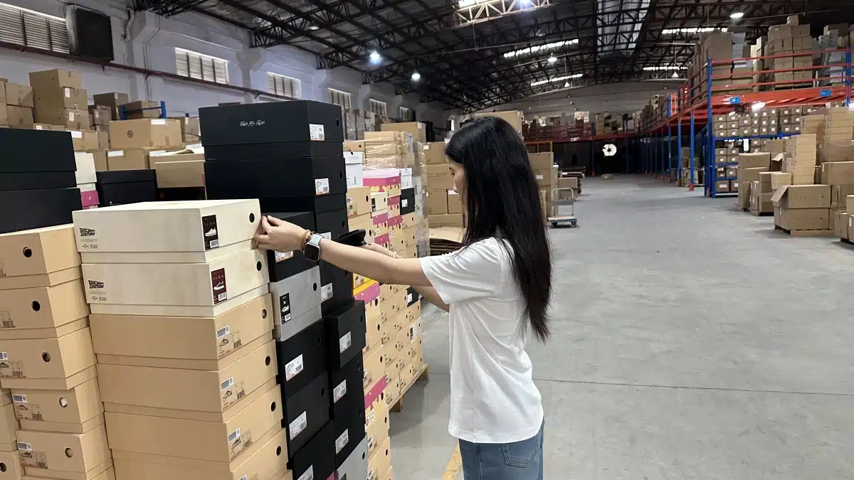 Warehouse worker organizing product boxes in a fulfillment facility, illustrating how inventory handling, storage volume, and labor affect warehousing service costs.