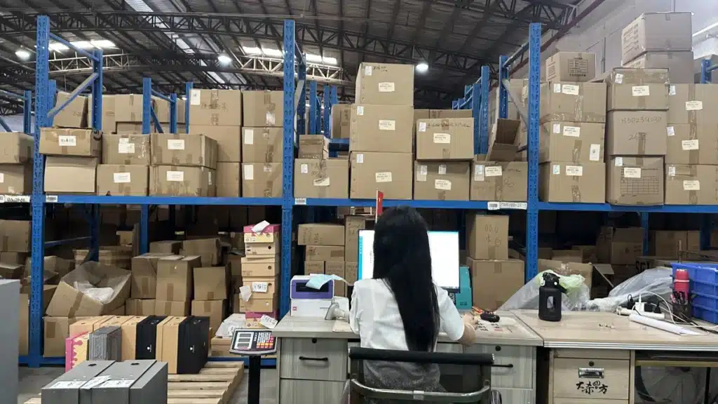 Warehouse employee processing eCommerce orders at a workstation surrounded by inventory, demonstrating order synchronization and WMS-based pick and pack fulfillment.