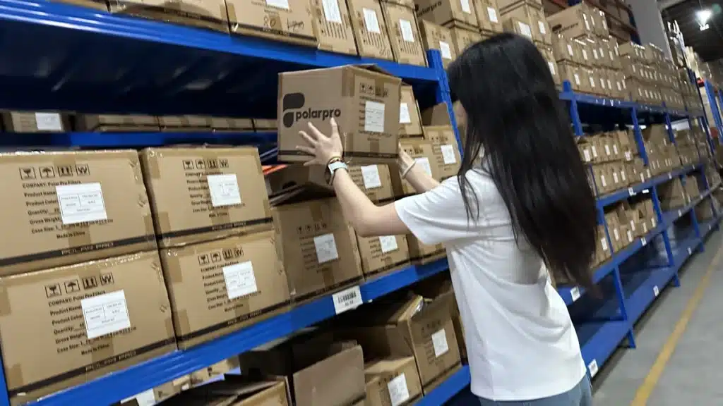 Warehouse worker picking a labeled carton from storage racks, demonstrating pick and pack operations that contribute to warehousing and fulfillment costs.