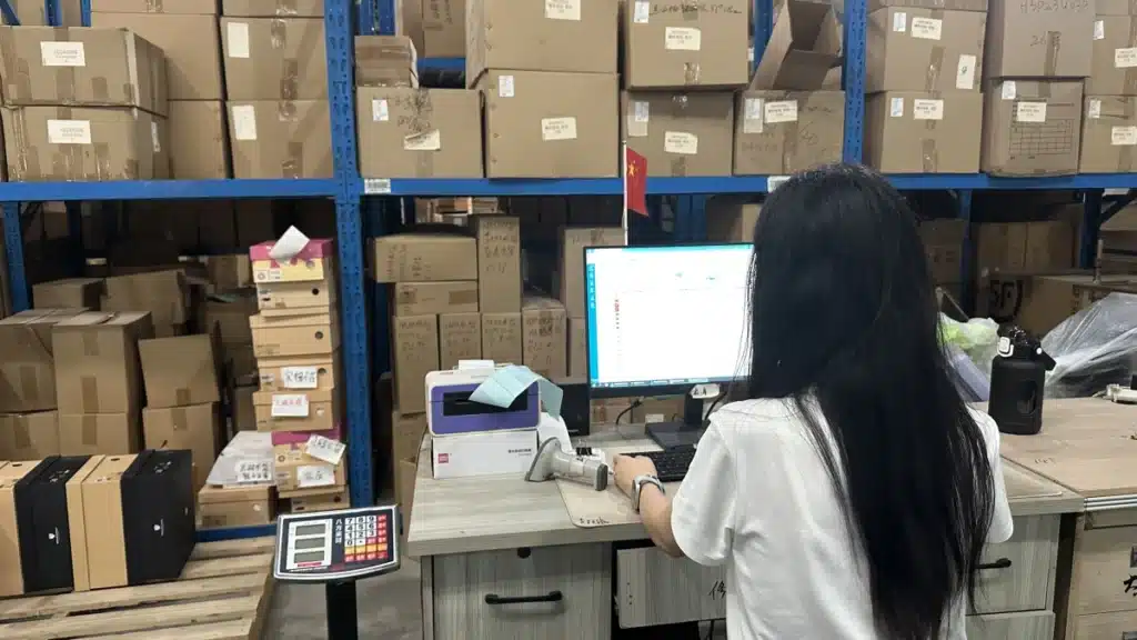 Warehouse employee using a computer and scanning equipment to manage inventory, demonstrating stock tracking and order processing in modern logistics warehousing.