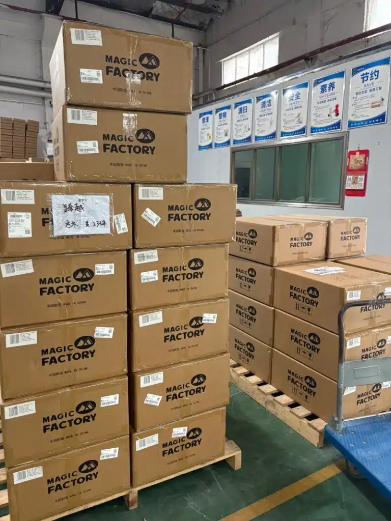 Stacked "MAGIC FACTORY" branded cardboard boxes on wooden pallets inside a warehouse, illustrating professional order fulfillment and inventory preparation for small business e-commerce shipping and logistics services