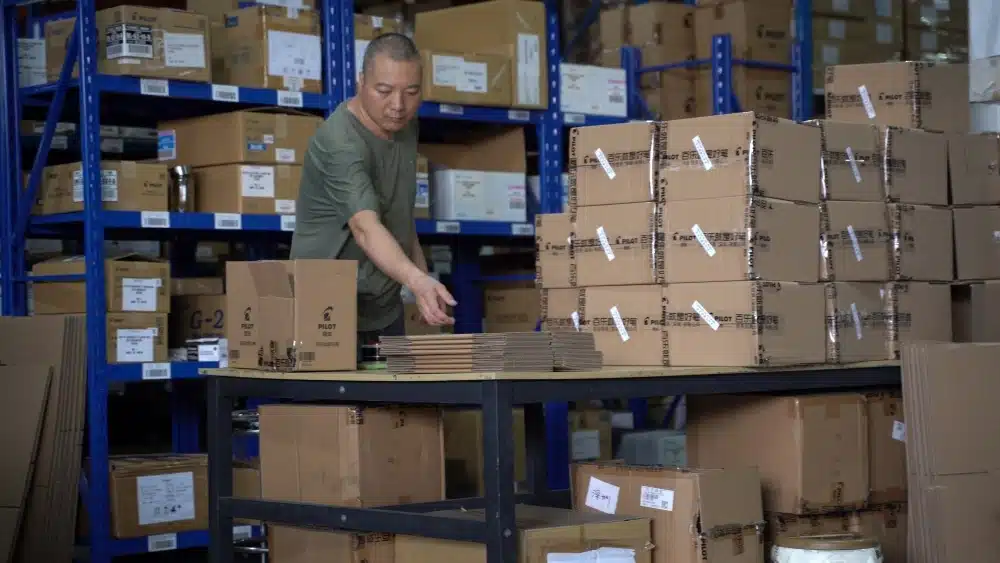 Warehouse worker preparing cardboard packages in a fulfillment center to support ecommerce carbon footprint calculation and sustainable logistics management