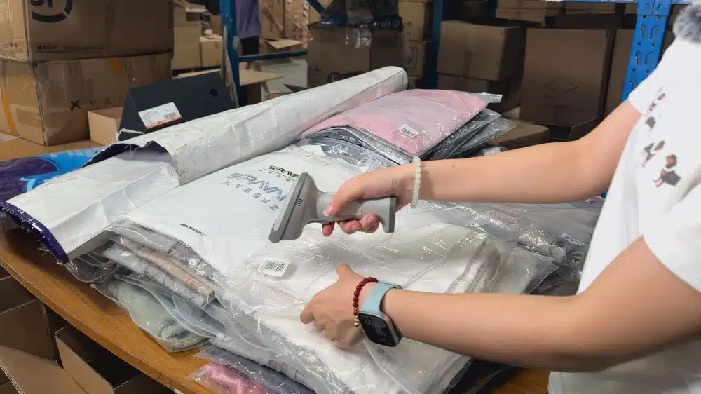 Warehouse worker packing apparel products for ecommerce fulfillment with organized inventory and order preparation workflow