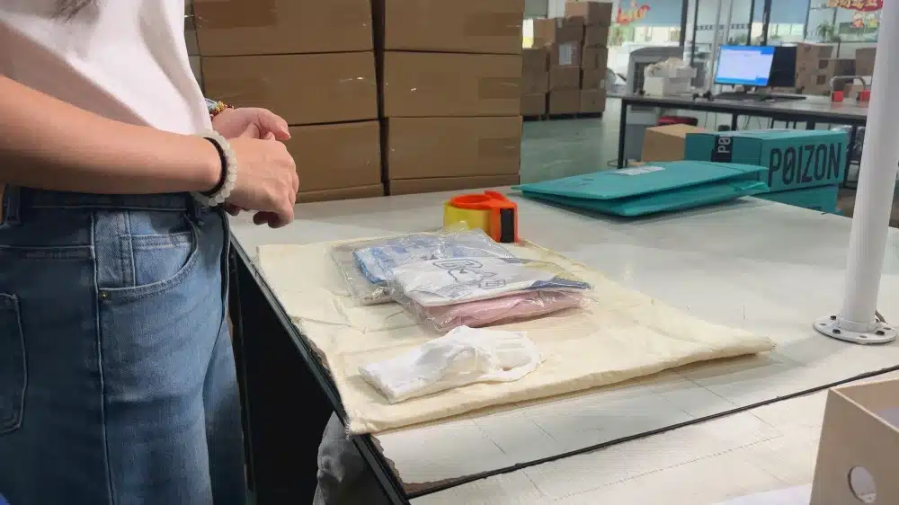Employee packing clothing products at a warehouse workstation for order fulfillment and logistics shipping
